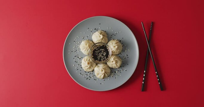 Composition of plate with dim sum dumplings and chopsticks with soy sauce on red background