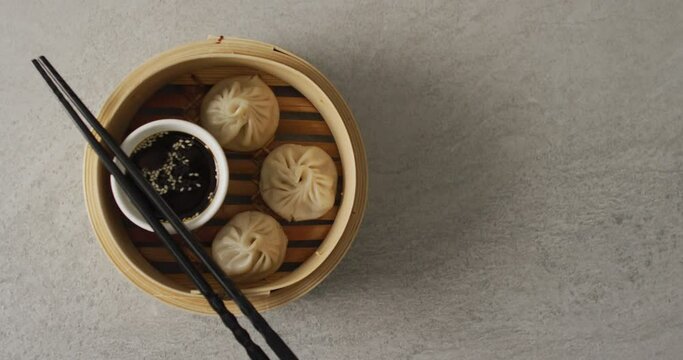 Composition of bamboo steamer with dim sum dumplings and chopstick with soy sauce on grey background
