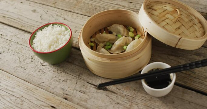 Composition of bamboo steamer with gyoza dumplings and soy sauce on wooden background