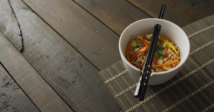 Composition of bowl of pad thai with chopsticks on wooden background