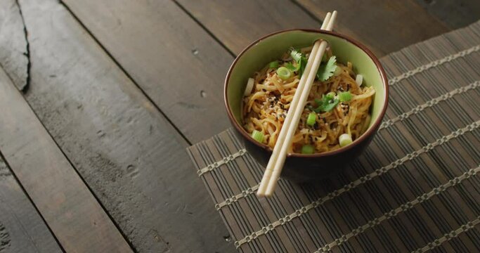 Composition of bowl of pad thai with chopsticks on wooden background
