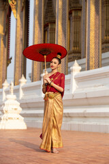 Full length portrait of smiling beauty young Asian woman wearing Thai traditional dress holding a...