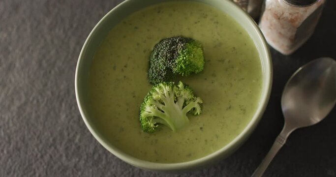 Video of cream broccoli soup in bowl on grey table with spoon and spices