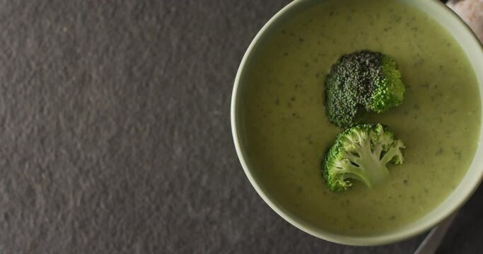 Video of cream broccoli soup in bowl on grey table with spoon and spices
