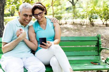 Fototapeta premium couple sitting on bench in park using phone