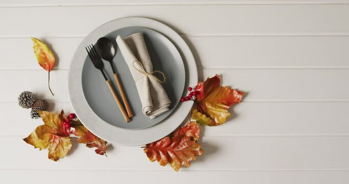 Video of plate with cutlery and autumn decoration with leaves on white surface