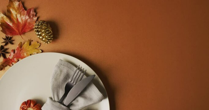 Video of plate with cutlery and autumn decoration with leaves on orange surface