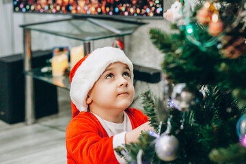 A boy in a Santa costume is decorating a Christmas tree