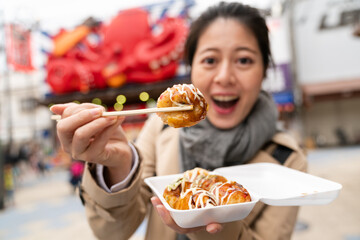 selective focus of delicious takoyaki octopus ball held on chopsticks by an amazed Asian Japanese...
