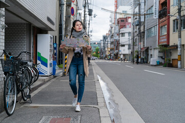 full length of Asian Taiwanese girl looking for destination using a route map while walking down a street in Osaka japan at spring time