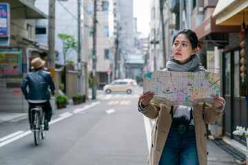 lost Asian Korean female visitor holding using a map to figure out where she is while walking on a...