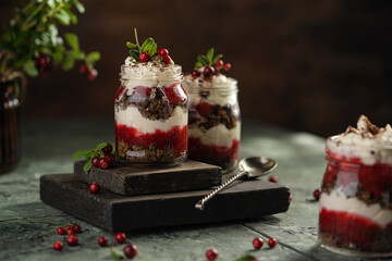 Latvian, scandinavian traditional rye whole grain bread layered dessert with whipped cream and cowberry jam served in glass jars on brown wooden board, table with berries, copy space. - obrazy, fototapety, plakaty