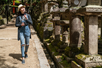 full length of curious Asian Chinese girl looking at Japanese traditional stone lanterns lined up along the path at kasuga Taisha Shinto shrine in nara japan on sunny day