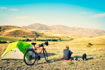 Caucasian man sit by touring bicycle in mountains on side of green tent have break time rest in...