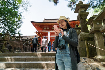 Asian Japanese girl backpacker consulting online travel info on mobile phone near a stone staircase while visiting kasuga taisha Shinto shrine in nara japan