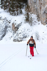 Fototapeta na wymiar young man in red brown clothes with backpack skiing near rocks and cliffs covered snow Active healthy lifestyle Winter sports Hiking