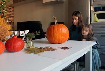 A little girl and an older sister make a Jack Lantern out of a large pumpkin, preparing for the Halloween holiday, autumn home and street decor