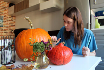 A brunette with long hair makes a sketch on a pumpkin, preparing for the Halloween holiday, making Jack's lamp for the autumn holiday, All Saints' Day