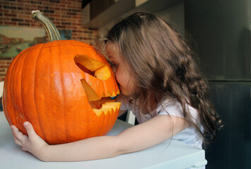 A little girl with long hair hugs a large pumpkin made for the Halloween holiday. The tradition of making Jack's lantern for the autumn holiday, All Saints' Day