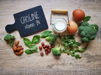 Foods high in choline with text Choline on black chalkboard. Choline is one of the most essential nutrients the human body needs.  Eggs, broccoli, nuts, milk, dairy, spinach, arugula...