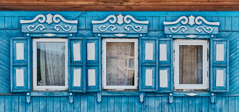 Old wooden blue windows with carved architraves and shutters on plank facade of house in Buryatia
