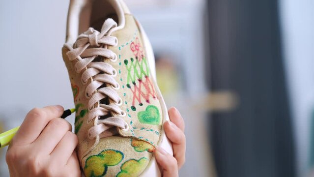 shoe design, female fashion designer draws modern print on sneakers with markers on fabric, creating a unique style, close-up