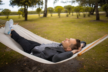 Handsome businessman with smartphone relaxing in hammock outdoors 