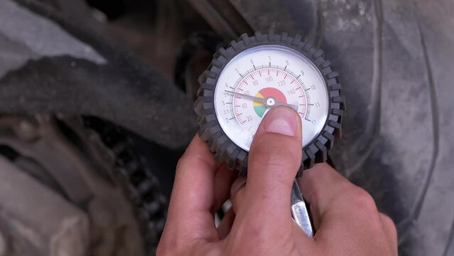 A Man Checks the Air Pressure in a Motorcycle Tire with a Pressure Gauge. Pressure manometer needle measures tire pressure. Driver in the garage checking the safety of motorcycle wheels before leaving