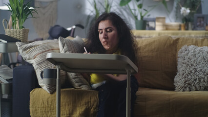 Woman with spinal muscular atrophy sitting on a couch at home at the table and drawing with digital pencil in her spare time