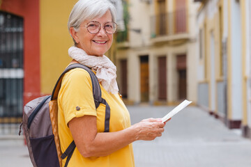 Attractive carefree senior traveler woman carrying backpack visiting the old town of Seville, smiling elderly lady enjoying travel and discovery
