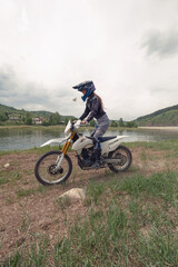 Obraz premium Beautiful female wearing helmet and moto protection turtle driving dirt motorcycle near the river