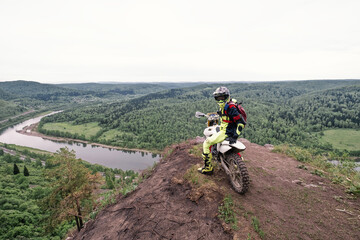 Motorcyclist posing on dirt motorcycle on the edge of cliff with gorgeous view of mountain valley