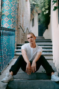 Young stylish male model sitting on the steps and posing on European city street