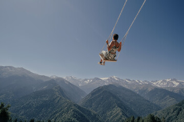 Naklejka na ściany i meble travel concept, Young beautiful woman flying on swing in blue sky over dizzying mountain gorge