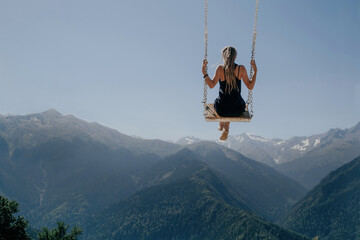 Young woman flying on swing in the sky over beautiful mountains, dream concept