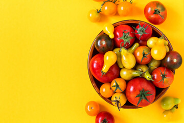 Bowl with tomatoes of various varieties and colors on a yellow background. Organic red tomatoes, yellow pear tomatoes, cherry tomatoes. Top view. Copy space.