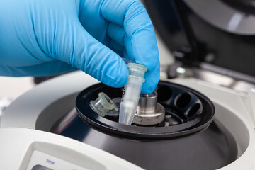 Closeup of a scientist hand placing a tube into an small table centrifuge. Spin column-based...