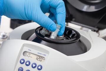 Closeup of a scientist hand placing a tube into an small table centrifuge. Spin column-based...
