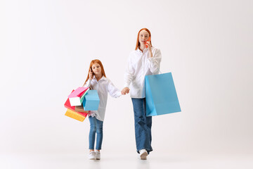 Busy ladies. Beautiful young redhaired mother and daughter going shopping with shopping bags. Concept of black Friday, cyber Monday, sales