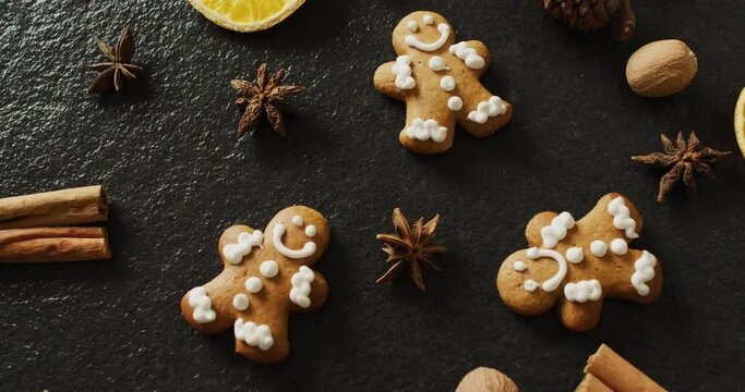Video of smiling gingerbread men and spices, slices of orange and nuts over black background