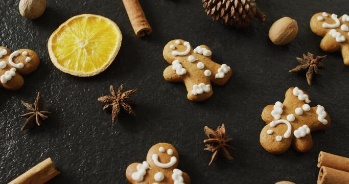 Video of smiling gingerbread men and spices, slices of orange and nuts over black background