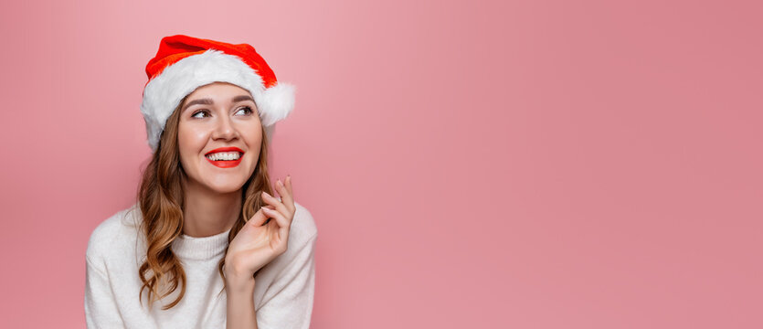 Close up portrait of young happy smiling woman in santa hat isolated on pink background in studio