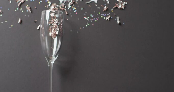 Video of champagne flute glass, with glitter confetti and silver stars on black, with copy space
