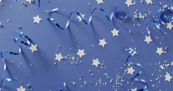 Video of multiple silver stars and party streamers scattered on blue background
