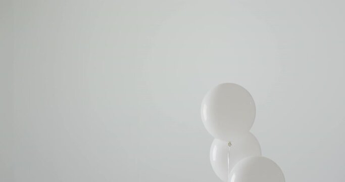 Video of three white balloons on white strings floating on white background, with copy space