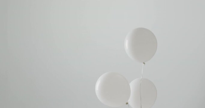 Video of three white balloons on white strings floating on white background, with copy space