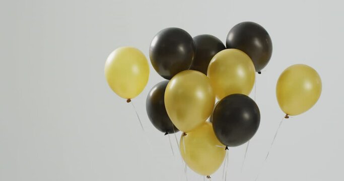 Video Of Black And Gold Balloons Floating On White Background, With Copy Space