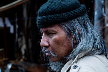 Close Up The face and eyes of a homeless old man leaning against the wall of an old building,...