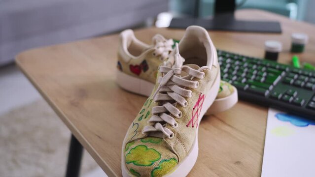 handmade shoes, worn pair of sneakers with updated design and print stand on the table, close-up