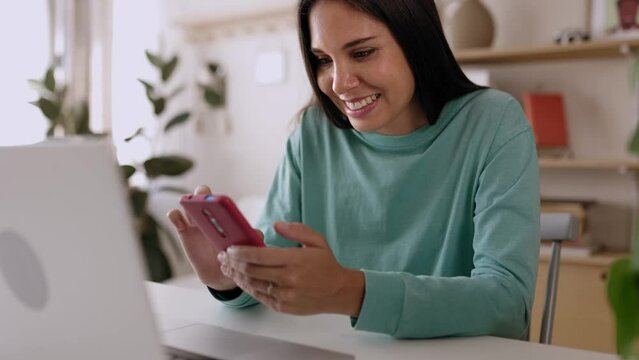 Young freelancer woman using mobile phone while working on laptop at home office. High quality 4k footage